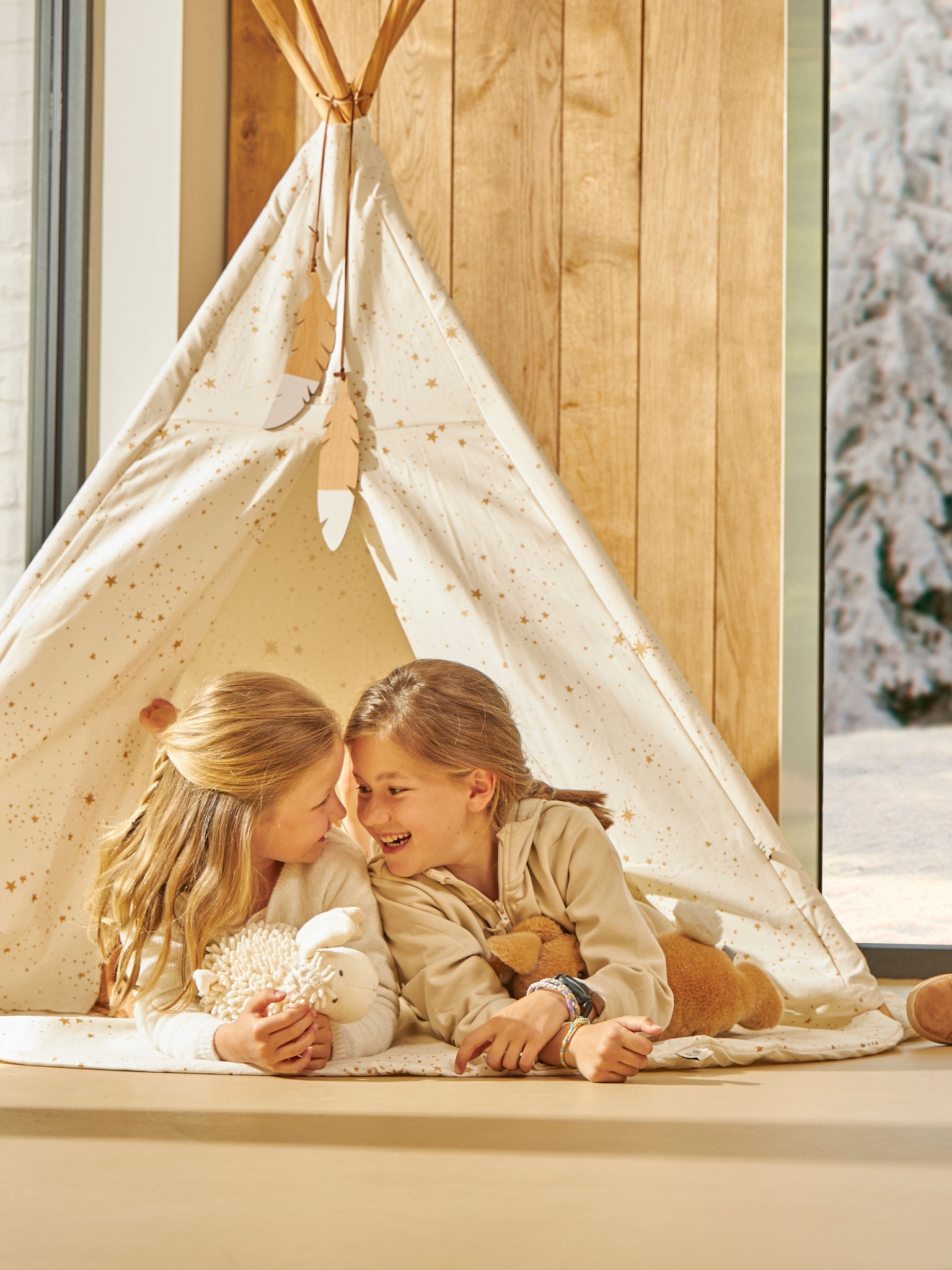 Две малки деца си играят щастливо в палатка в дома си при идеална температура