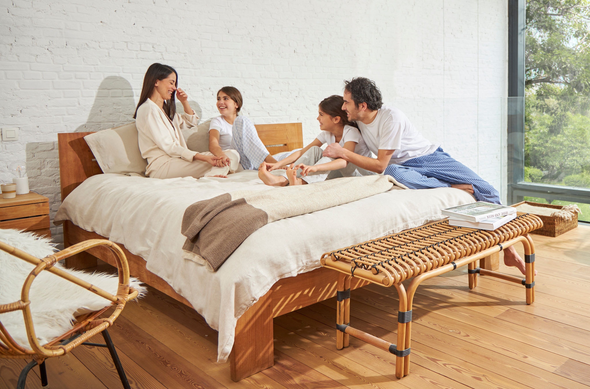 Жена и мъж, седящи на легло с две млади момичета, спокойни, смеещи се и наслаждаващи се на здравословен въздух.