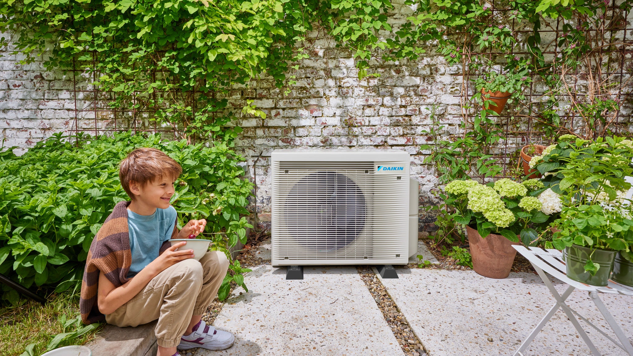 Дете близо до външно тяло на хибридна термопомпа Daikin, съчетаваща енергийна ефективност с приятна градинска обстановка