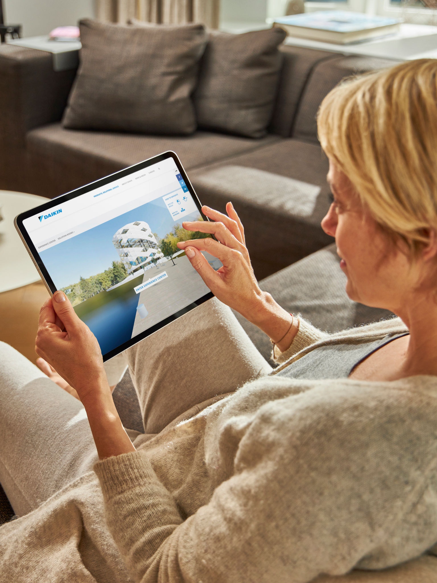 Жена, която седи на диван и разглежда климатици във Virtual Experience Center на своя таблет