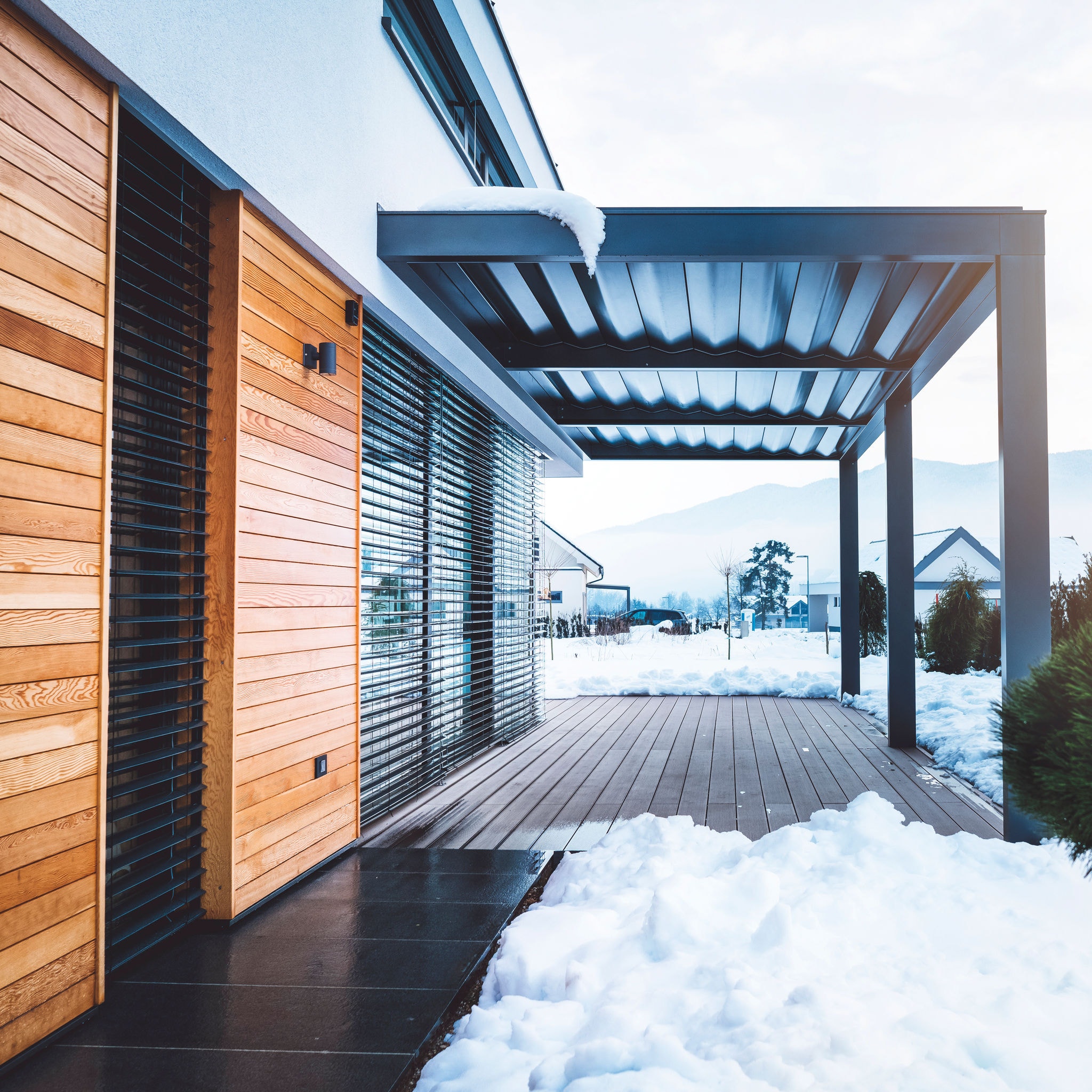 Modern building with hard top pergola over the patio. White facade and wooden facade compliment each other, combined with large windows with metal frames, making the design simple and everlasting.  This luxurious house makes a perfect family home with plenty of natural light.