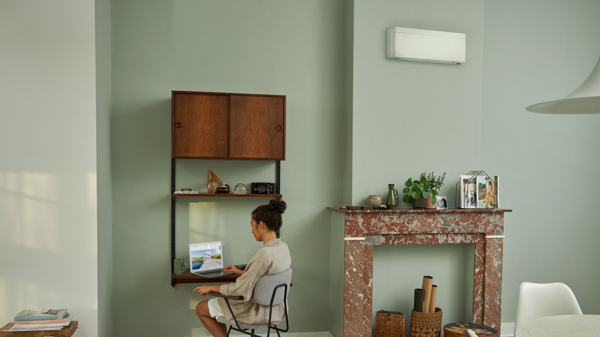 Жена, посещаваща Daikin Virtual Experience Center чрез своя лаптоп на малкото си бюро в красиво декорирана всекидневна